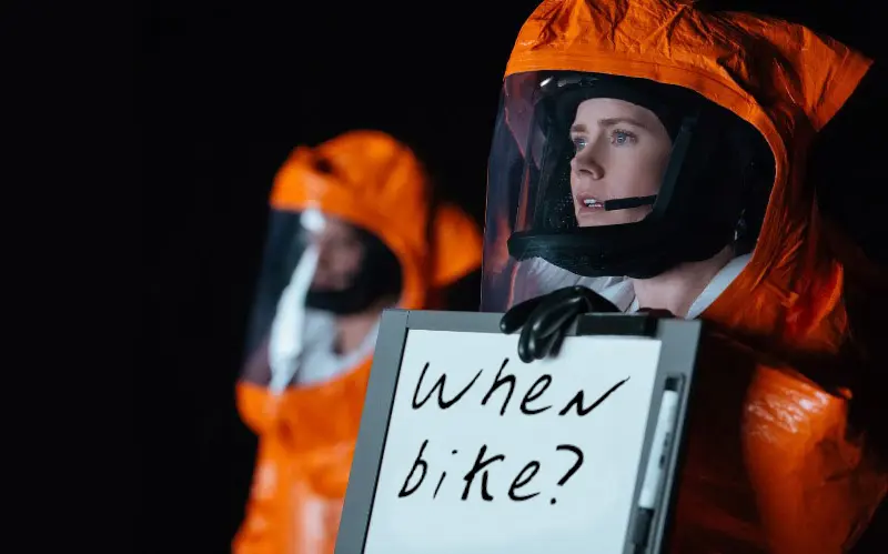 header image from a scene in the movie Arrival when Amy Adams is holding a sign that says 'when bike?'